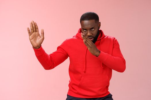 Guy knows asian fighting skills. Portrait serious-looking funny african-american young man perform martial arts standing kung-fu karate pose raised palms, pink background, better not mess with me.