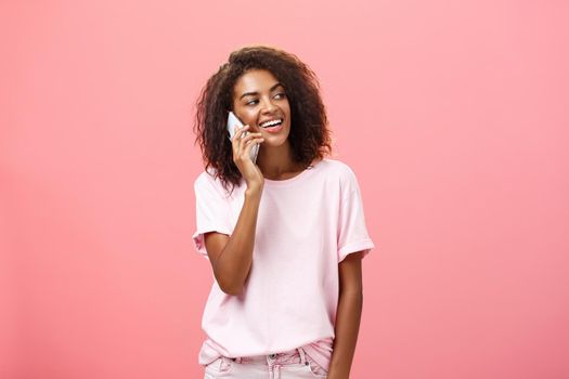 Woman calling boyfriend come pick her up after practice standing on street carefree and chill gazing right with broad satisfied smile holding smartphone near ear posing over pink background. Technology and emotions concept