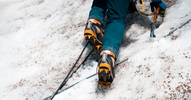 A young man traveler uses an ice ax while hiking in the mountains, a hiker with climbing equipment, in a crampons on boots climbs to the top of a snow-capped mountain.