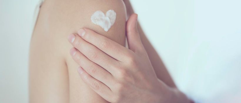 A young girl applies a moisturizer to her skin, a woman gently cares for her body, depicts a heart with a cream, taking care of herself, beauty and health.