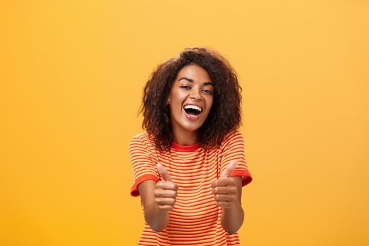 Woman surely knows how boost mood. Portrait of friendly-looking stylish and outgoing african american girlfriend with curly hairstyle showing thumbs up in like and approval agreeing to friend idea.