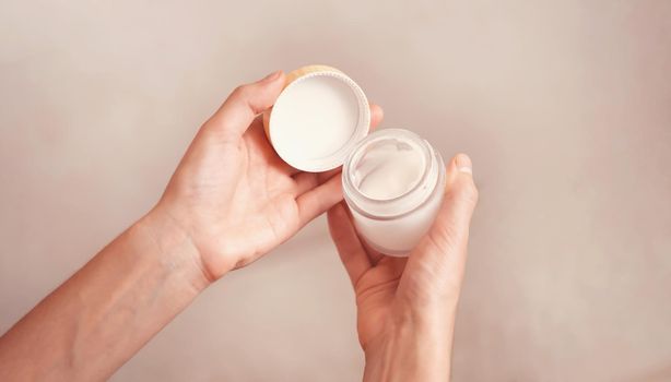 Young female hands hold a jar of moisturizing cream to maintain health, softness of the skin, the woman takes care of her health and beauty.