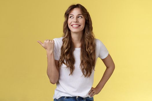 Satisfied carefree cheerful attractive european woman show thumb up pointing left turn aside pleased delighted expression discuss recent awesome purchase showing friend new car yellow background. Lifestyle.