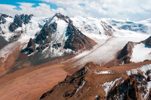 Rocks of the highlands, snow-capped peaks of mighty mountains in the clouds, a stunning view of the glacier from above.