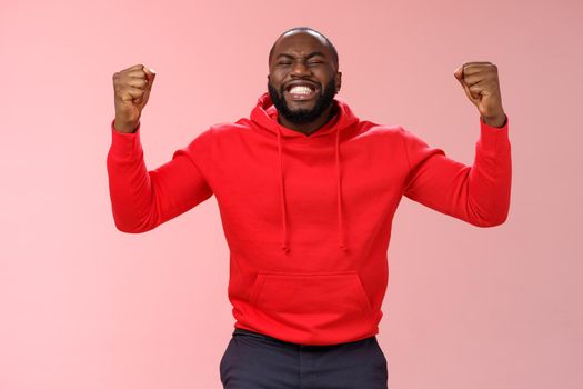 Happy thankful young african american bearded man thank god for son close eyes joyfully smiling clench fists celebrating triumphing dream come true accomplish goal, cheering victory.