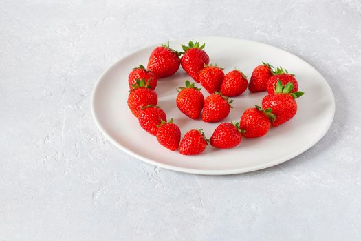 white plate with strawberries in a heart shape, concept of Valentine's Day, top view, copy space
