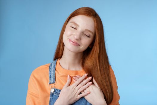 Dreamy touched romantic ginger girlfriend close eyes recalling heartwarming romance touch heart palms pressed chest smiling tenderly feel love care sympathy express affection, blue background.