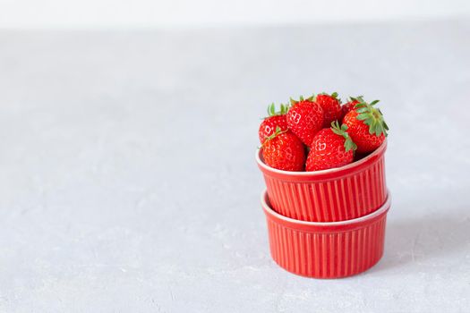red bowls full of fresh strawberries, side view, light grey background, selective focus, copy space