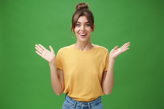 Amazed and surprised woman reacting to astonishing gift raising hands near shoulders smiling happily at camera being delighted and pleased with awesome surprise made by friends over green wall. Lifestyle.