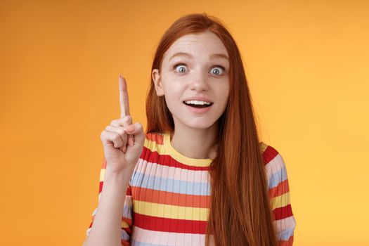 Great idea striked mind. Attractive excited surprised redhead woman open mouth smiling amused raise index finger eureka gesture stare camera shocked found solution have perfect plan.