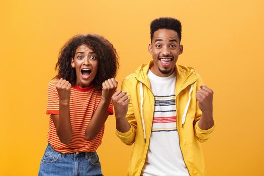 Two friends cheering and supporting mate on competition yelling joyfully clenching fists in supportive geture smiling broadly waiting with amazement and excitement for win and victory. Lifestyle.