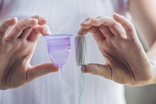 Young woman hands holding different types of feminine hygiene products - menstrual cup and tampons.