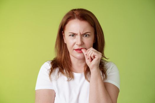 Confused puzzled redhead middle-aged mother perplexed look troubled solving troublesome situation pondering solution biting thumb nail frowning intense stare camera thinking thoughtfully.