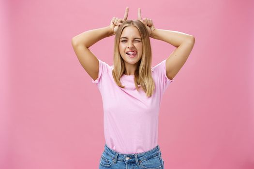 Stubborn girl never let down on dreams. Charming excited and carefree optimistic young woman with tan and fair hair winking showing tongue playfully holding index fingers on head like horns. Body language and emotions concept