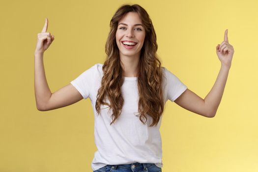 Cheerful amused happy lively young girl long curly haircut raise hands pointing up smiling toothy happily camera introduce excellent variant suggest you click site link advertising yellow background. Lifestyle.