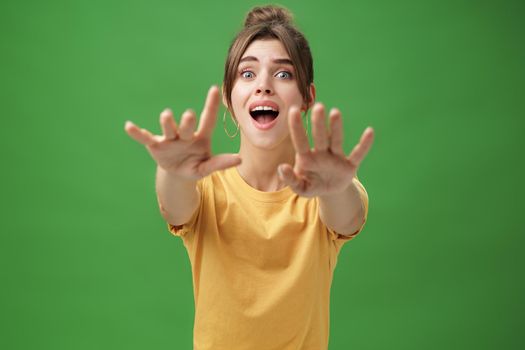 Excited and addicted goog-looking young woman reaching hands forward to camera with reckless look wanting grab something she desire seeing thing she wanted for long time over green background. Lifestyle.