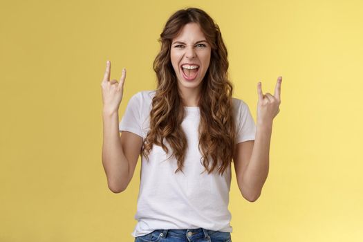 Going wild. Daring amused good-looking european curly-haired girl acting thrilled excited having fun enjoy awesome concert show yeah rock-n-roll heavy metal gesture grimacing satisfied.