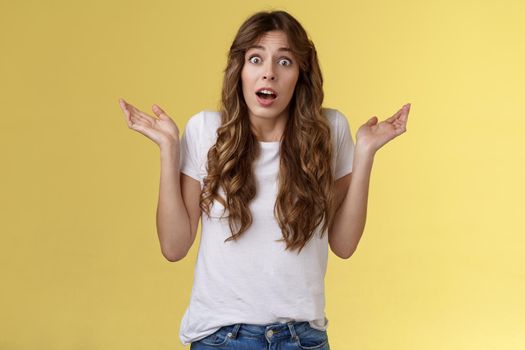 I not know. Clueless confused cute nervous young woman shrugging hands raised sideways full disbelief questioned expression lift eyebrows puzzled unable answer question stand yellow background.