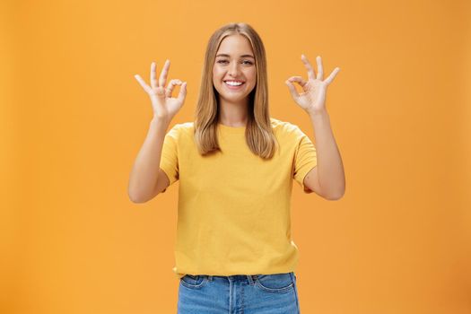 Optimistic charming woman with fair hair and no make-up in yellow t-shirt showing okay or approval gesture assuring everything ok and nothing to worry she can handle project alone, smiling confident. Emotions and body language concept