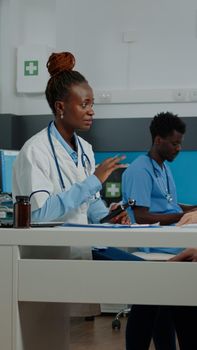 African american doctor holding medical otoscope on old man to examine ear infection in cabinet. Black otologist using tool while senior patient sitting at desk waiting for diagnosis