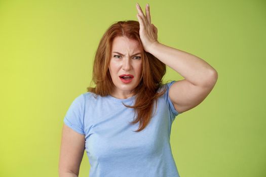 Ouch you kick my head. Frustrated concerned upset middle-aged redhead woman look shocked distressed touch temple complain kid shoot ball her face stand disappointed green background. Copy space