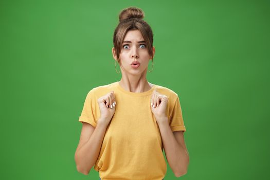 Studio shot of silly insecure and timid young wife feeling troubled and concerned, pressing hands to body folding lips and frowning looking scared and nervous facing troublesome situation, worry. Body language and emotions concept