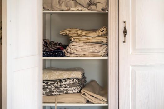 A beautiful white wooden cabinet with door knobs in a vintage retro style, inside are neatly folded towels and bed linens in beige shades.