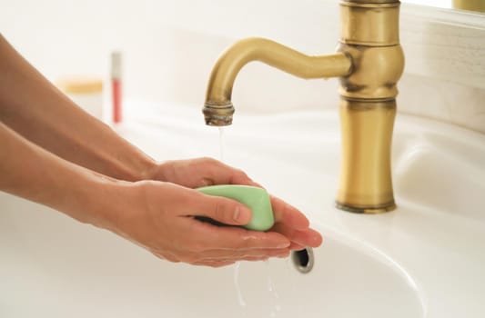 A young girl washes her hands thoroughly with soap under water in the bathroom, close-up view.