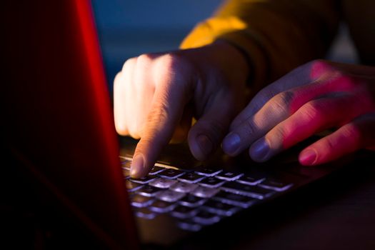 Male hands are typing on a laptop keyboard, a man works, develops a business, studies, plays a computer game at night. Close-up view.