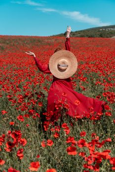 Young woman stands with her back in a long red dress and hat, posing on a large field of red poppies.