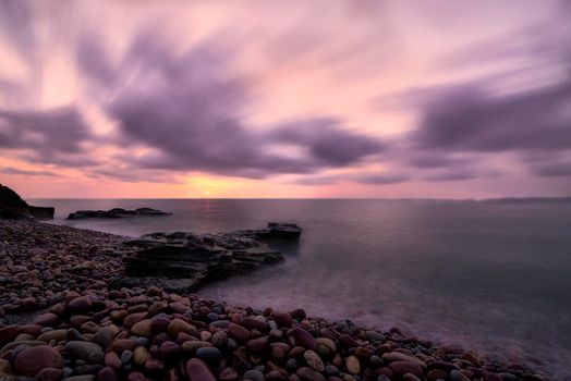 Sunrise on rocky beach in long exposure. Clouds outside, lonely beach, silk effect, orange colours.