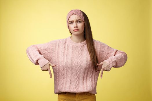 Why me, gosh. Gloomy upset complaining cute glamout young european girl in casual sweater, headband frowning, whining grimacing displeased pointing down, unhappy see lots work over yellow wall.