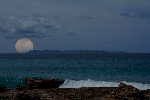 Full moon rising behind small island. Mediterranean. Balearic Islands, clouds, calm waters, empty space.