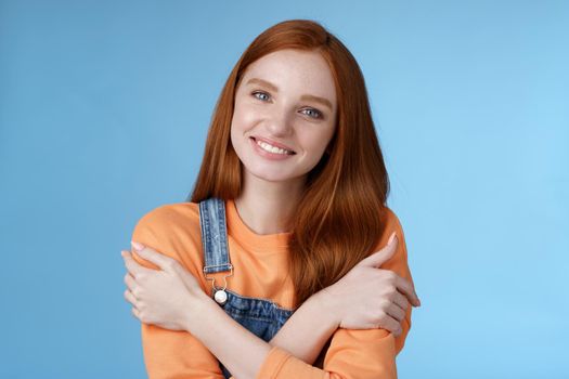 Lifestyle. Tender silly redhead girl standing blue background smiling joyfully hugging arms crossed body feel chilly grinning delighted talking boyfriend romantic date asking lend jacket cold summer evening.