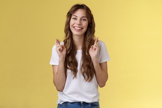 Girl faithfully believe dream come true hopefully awaiting positive results smiling broadly cross fingers good luck implore god good news stand excited optimistic yellow background.
