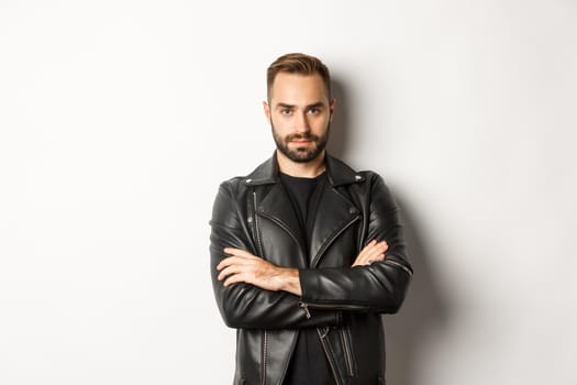 Handsome man wearing leather jacket, looking confident at camera, standing over white background.