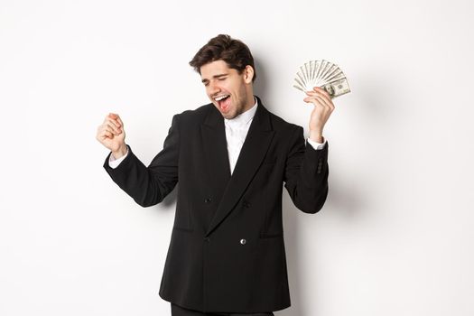 Portrait of handsome and successful businessman in suit, dancing with money, standing against white background.