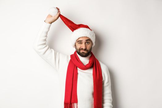 Christmas party and celebration concept. Sad guy taking-off Santa hat and grimacing, looking upset, standing against white background, bad New Year.