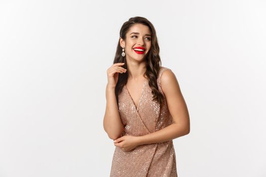 Elegant woman standing in evening dress and makeup, laughing and celebrating New Year, wearing outfit for formal party, standing over white background.