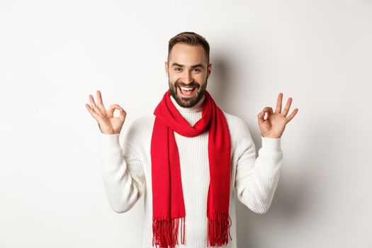 Winter holidays and shopping concept. Excited gay man celebrating christmas, showing okay signs and smiling self-assured, standing over white background.