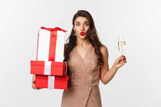 New Year, Christmas and celebration concept. Elegant woman in luxury dress and red lipstick, holding gifts and drinking champagne on party, standing over white background.