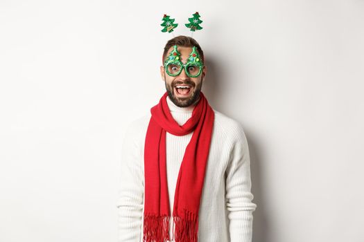 Christmas, New Year and celebration concept. Handsome bearded man looking surprised, wearing party glasses and accessory, white background.