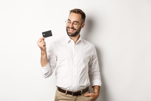 Handsome businessman showing his credit card, looking satisfied, standing over white background.