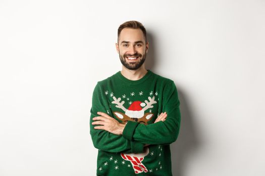 New Year party and winter holidays concept. Happy bearded man in funny christmas sweater standing against white background.