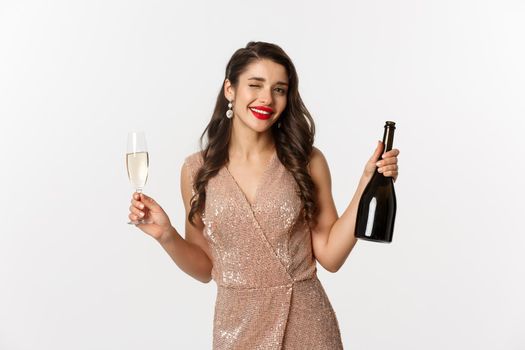 Winter holidays celebration concept. Beautiful woman enjoying Christmas and New Year party, drinking champagne and winking at camera, standing in elegant dress.