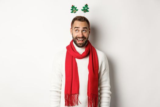 Christmas holidays. Excited man celebrating winter holidays, wearing New Year party accessory and red scarf, standing against white background.