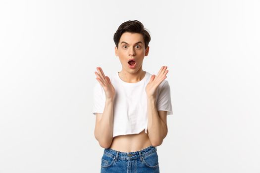 Lgbtq and pride concept. Image of surprised queer guy clap hands and looking in awe at camera, standing in crop top against white background.