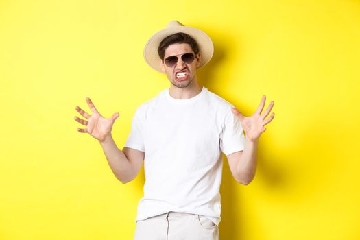 Tourism, travelling and holidays concept. Sassy young man on vacation, showing something big and clenching teeth, standing in sunglasses and summer hat.