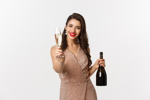 Winter holidays celebration concept. Beautiful woman in elegant dress giving you glass of champagne on Christmas party, standing over white background.