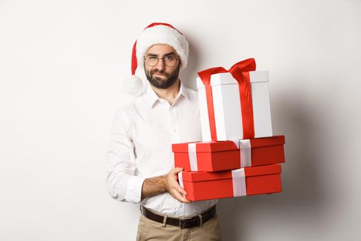 Merry christmas, holidays concept. Thoughtful man holding xmas gifts and looking suspicious at camera, celebrating New Year, white background.
